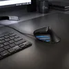 A close-up shot of a black ergonomic mouse with blue LED lights, placed on a black desk next to a black keyboard. Produktbild-Vorschau