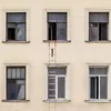 A red ladder is positioned between two windows on a building's facade. Voir les images du produit