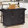 A dark brown kitchen cart with a stainless steel top is shown in a kitchen setting. It has two doors, three drawers, and a pull-out drawer on the left. Various food items and a bottle of wine are placed on top of the cart. Podgląd zdjęcia produktu