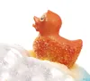 A close-up of a small, orange, glitter-covered rubber duck sitting on a white, snowy surface. Voir les images du produit