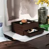 A jewelry box with items on top and in a drawer, placed on a white surface next to a vase of flowers and a book. Voir les images du produit