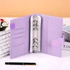 An open purple binder notebook with a keyboard and flowers in the background. Voir les images du produit
