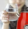 A person holds a glass of water next to a red electric kettle. Podgląd zdjęcia produktu