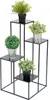 A black metal plant stand with four tiers, holding four artificial plants in pots. Produktbild-Vorschau