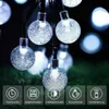 A string of solar-powered LED lights with bubble-like glass bulbs, displayed outdoors on grass, with feature icons at the bottom. Produktbild-Vorschau