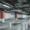 An empty underground parking garage with concrete floors, white walls, and exposed ceiling infrastructure. Produktbild-Vorschau