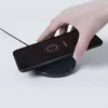 A hand is placing a smartphone onto a black wireless charging pad. Produktbild-Vorschau