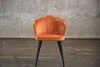An orange velvet chair with black legs is shown against a concrete wall and wooden floor.