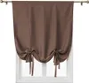 A brown tie-up Roman shade curtain hanging on a window rod over a window. Náhled obrázku produktu