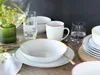 A table setting with white porcelain dishes, glasses of water, and a vase with yellow flowers. Produktbild-Vorschau