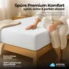 A person sitting on a bed with a white fitted sheet. Produktbild-Vorschau