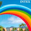 Children's hands reaching up towards a rainbow sprinkler with water spraying down, with palm trees and mountains in the background. Produktbild-Vorschau