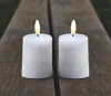 Two white LED candles with lit flames sit on a wooden surface. Produktbild-Vorschau