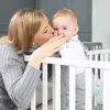 A mother kissing her baby in a crib. Náhled obrázku produktu