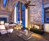 A cozy, rustic living room with a stone fireplace, wooden beams, and large windows. Podgląd zdjęcia produktu