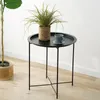 A small black round side table with a plant and a cup on it, placed on a wooden floor next to a larger plant. Produktbild-Vorschau