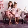 Two young girls sitting on a pink couch, holding stuffed toys. Produktbild-Vorschau