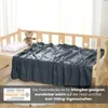 A dark gray fleece blanket is draped over a wooden crib, with a teddy bear and a pillow on the crib. Produktbild-Vorschau