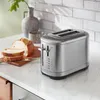 A stainless steel toaster sits on a marble countertop next to sliced bread and a vase with a plant. Anteprima dell’immagine prodotto