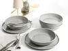 A set of grey ceramic bowls and plates arranged on a white surface, with a napkin and cutlery in the foreground. Produktbild-Vorschau