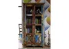 A rustic, multi-colored wooden display cabinet filled with books and decorative items, set against a patterned wallpaper. Anteprima dell’immagine prodotto