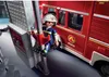 A toy firefighter figure is sliding down a pole next to a toy fire truck. Produktbild-Vorschau