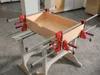 A wooden drawer is being assembled and held together by several clamps on a workbench. Náhľad obrázku produktu