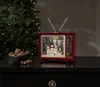 A festive Christmas scene with a retro television decoration, a bowl of nuts, and a decorated Christmas tree in the background. Podgląd zdjęcia produktu