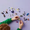 A child's hands are assembling LEGO minifigures on a purple background. Náhled obrázku produktu