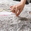 A hand is shown pressing into a soft, shaggy, gray rug. Náhled obrázku produktu