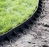 A close-up view of black plastic lawn edging installed along the edge of a grassy area. Produktbild-Vorschau