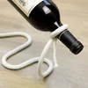 A wine bottle is held up by a rope wine bottle holder, which is placed on a wooden surface. Produktbild-Vorschau