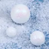 Three white glittery spheres are scattered on a blue surface covered with artificial snow. Produktbild-Vorschau