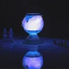 A glowing, spherical object with a blue base sits on a reflective surface in a dark room. The object appears to be a magical potion maker with light emanating from within. Náhled obrázku produktu