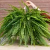 A person is holding a large, lush green fern plant in a hanging basket. Podgląd zdjęcia produktu