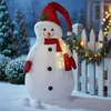A festive snowman decoration stands in the snow next to a white picket fence adorned with Christmas lights and garland. Voir les images du produit