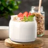 A serving of yogurt with granola and strawberries in a glass jar, placed on a wooden surface. Produktbild-Vorschau