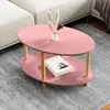 A pink oval coffee table with wooden legs is placed on a gray rug next to a white sofa. A book and a small vase with dried flowers are on the table. Podgląd zdjęcia produktu