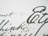 A close-up of a white fabric with black script-like text printed on it. Produktbild-Vorschau
