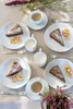 A table setting with slices of chocolate cake, diced apples, and cups of coffee, arranged on plates with forks. Produktbild-Vorschau