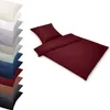 A stack of folded bedding in various colors is shown on the left, with a burgundy duvet and pillow set displayed prominently on the right. Produktbild-Vorschau