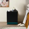A black nightstand with LED lighting is placed next to a bed in a bedroom. Produktbild-Vorschau