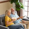 An elderly couple is sitting on a sofa, watching TV and eating popcorn. Produktbild-Vorschau