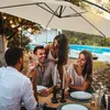 People enjoying a meal outdoors under a large umbrella, with a swimming pool in the background. Náhled obrázku produktu