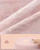 Close-up of textured pink fabric, with a bottom section showing a pink stool with a damp spot being wiped by a hand. Náhled obrázku produktu