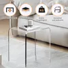 A clear acrylic side table with a book and candle on top, placed on a rug next to a sofa. Four circular icons with text are overlaid on the top left of the image, highlighting product features. Produktbild-Vorschau