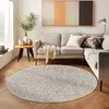A circular rug is placed on a wooden floor in front of a sofa in a living room. Produktbild-Vorschau