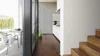 Interior view of a modern home with a kitchen and dining area visible through large glass doors, and a wooden staircase in the foreground. Náhled obrázku produktu