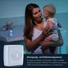 A mother holding a baby in a dimly lit room, with a product shown in the foreground. Voir les images du produit