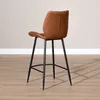 A brown leather bar stool with black metal legs is shown from the side against a light gray wall and a wooden floor. Produktbild-Vorschau